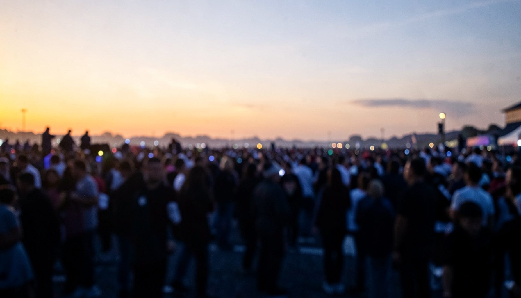 A wide atmospheric photograph of a large public gathering at dusk, with soft amber and navy tones, blurred crowd silhouettes